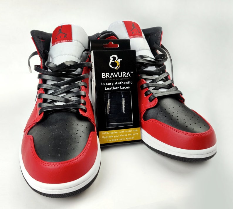 May include: A pair of red and black sneakers with black leather laces. The laces are branded with the text "BRAVURA&trade; Luxury Authentic Leather Laces".