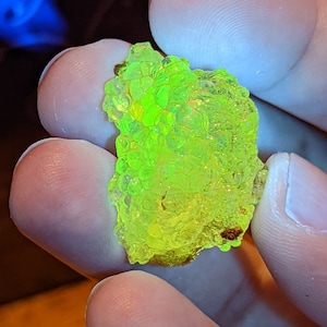May include: A close-up of a bright green, translucent, irregularly shaped rock with a bubbly texture. The rock is being held in a hand.