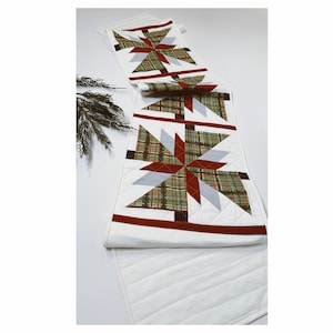 Peut inclure: Un chemin de table blanc avec un motif matelassé composé de trois motifs en étoile rouge, vert et gris. Le chemin de table est parfait pour ajouter une touche festive à votre table de fête.