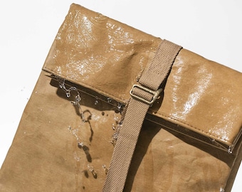 May include: A brown waterproof bag with a canvas strap and a brass buckle. Water droplets are visible on the surface of the bag.