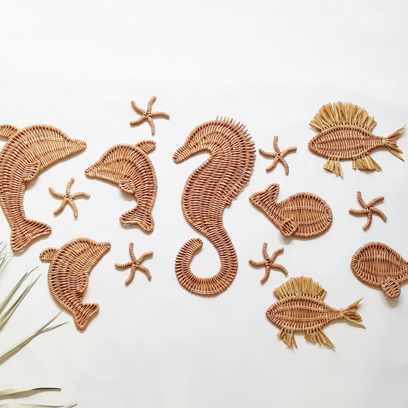 May include: A set of woven sea creature wall decor, including dolphins, a seahorse, starfish, and fish. The decor is made of natural materials and has a light brown color.