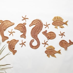 May include: A set of woven sea creature wall decor, including a seahorse, dolphins, starfish, and fish. The decor is made of natural materials and has a light brown color.