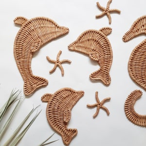 May include: A set of woven wicker wall decor featuring dolphins and starfish. The dolphins are in a light brown color and the starfish are in a slightly darker brown color.