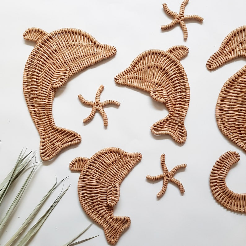 May include: A set of woven wicker wall decor featuring dolphins and starfish. The dolphins are in a light brown color and the starfish are in a slightly darker brown color.