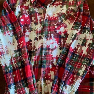 May include: Red and green plaid flannel shirt with white bleach splatters. The shirt has a button-up front and long sleeves. The brand label reads "Magellan".