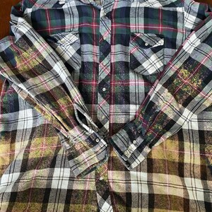 May include: A green, red, and white plaid flannel shirt with a faded, bleached look. The shirt has a button-down front and long sleeves.