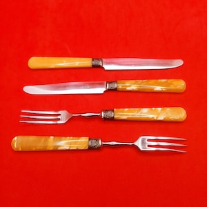 Peut inclure: Quatre couverts avec des manches de couleur ivoire et des lames argentées. La coutellerie comprend deux couteaux à beurre et deux fourchettes.