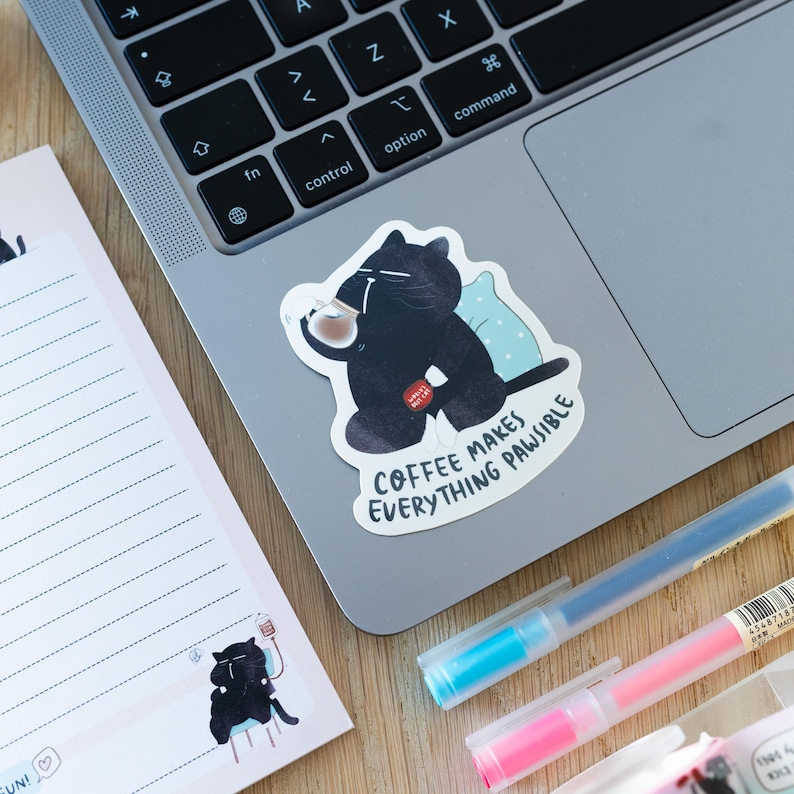 Pu&ograve; includere: Un adesivo di un gatto nero con una tazza di caff&egrave; nella zampa, seduto su un computer portatile. L'adesivo dice "Il caff&egrave; rende tutto possibile."