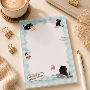 Op de afbeelding: Een rechthoekig notitieblok met een lichtblauwe en witte ruitjesrand en een geschulpt wit midden. Het notitieblok bevat illustraties van zwarte katten, koffiekopjes en de tekst "MOCHA CAT", "POWERED BY CATS AND COFFEE" en "MOONARIESILLO.COM".