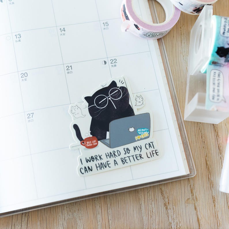 Pode incluir: Um autocolante com um gato preto de &oacute;culos a trabalhar num port&aacute;til. O texto diz: "I WORK HARD SO MY CAT CAN HAVE A BETTER LIFE." Tamb&eacute;m s&atilde;o vis&iacute;veis rolos de fita washi e um calend&aacute;rio.