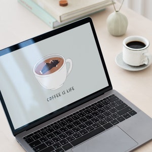 Op de afbeelding: Een laptop met een grijze buitenkant en een zwart toetsenbord. Het scherm toont een cartoonafbeelding van een kopje koffie met een slapende kat erin. De tekst "COFFEE IS LIFE" wordt onder de afbeelding weergegeven.