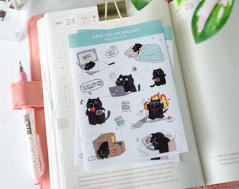 May include: A planner is open to a page dated September 24th, with a sticker sheet featuring black cat illustrations. The stickers depict cats in various work-related scenarios, with the text "WORK LIFE (UN)BALANCE". A pink pen and washi tape are also visible.