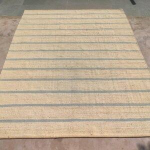 May include: A natural fiber rug with a striped pattern. The rug has a light beige background with blue stripes.