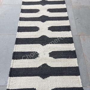 May include: Black and white striped rug with a geometric pattern. The rug is made of natural fibers and has a jute border.