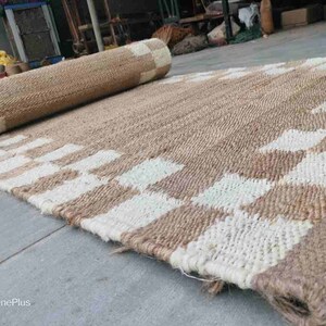 K&ouml;nnte beinhalten: Ein Naturfaser-Teppich mit einem karierten Muster in Beige und Wei&szlig;. Der Teppich ist aus gewebtem Jute gefertigt und hat eine nat&uuml;rliche, erdige Optik.