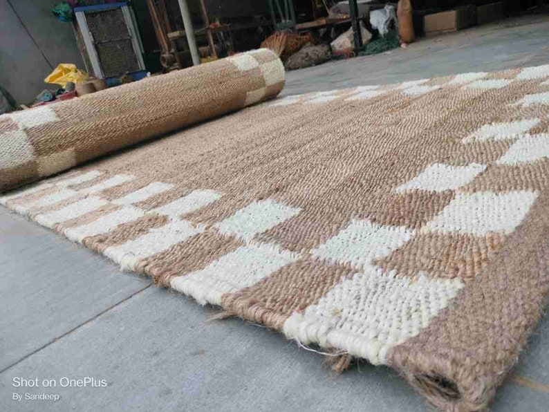 K&ouml;nnte beinhalten: Ein Naturfaser-Teppich mit einem karierten Muster in Beige und Wei&szlig;. Der Teppich ist aus gewebtem Jute gefertigt und hat eine nat&uuml;rliche, erdige Optik.