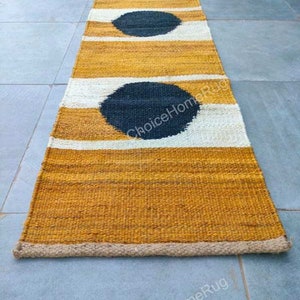 May include: A long, narrow, woven rug with a natural, beige color and black circles. The rug has a white border and is made of natural fibers.