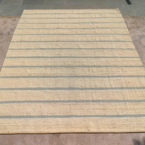 May include: A natural fiber rug with a striped pattern. The rug has a light beige background with blue stripes.