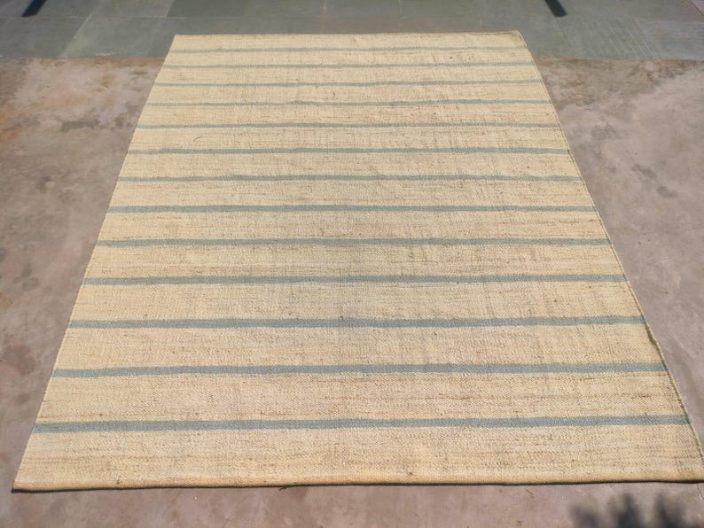 May include: A natural fiber rug with a striped pattern. The rug has a light beige background with blue stripes.