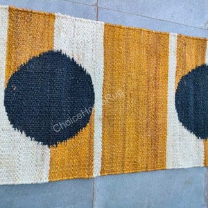 May include: A long, narrow rug with a striped pattern in white, yellow, and black. The rug has two large black circles on it.