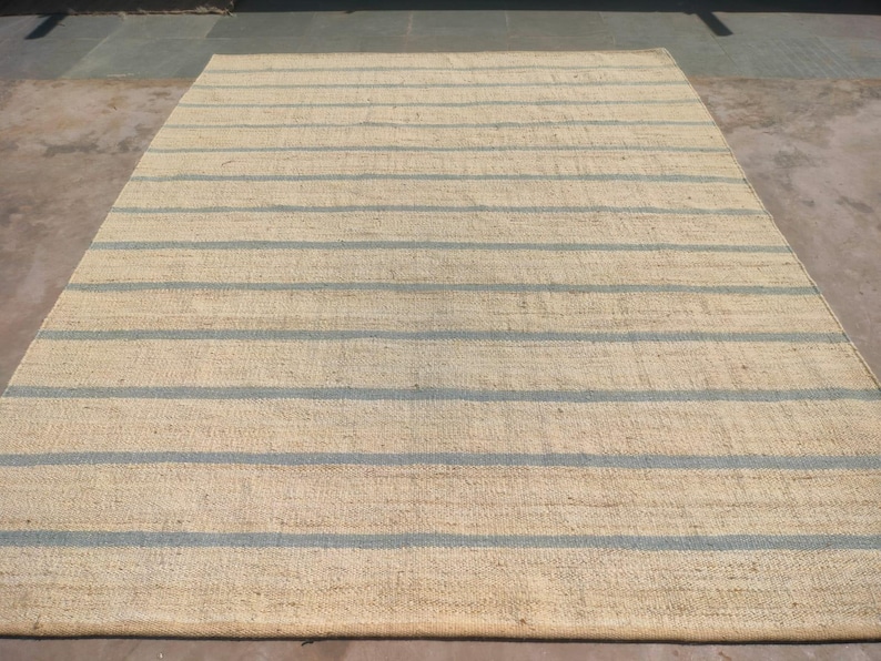 May include: A natural fiber rug with a striped pattern. The rug is made of a light beige material with blue stripes.