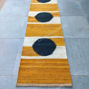 May include: A long, narrow rug with a mustard yellow background and white stripes. Three black circles are woven into the rug, creating a modern geometric pattern.