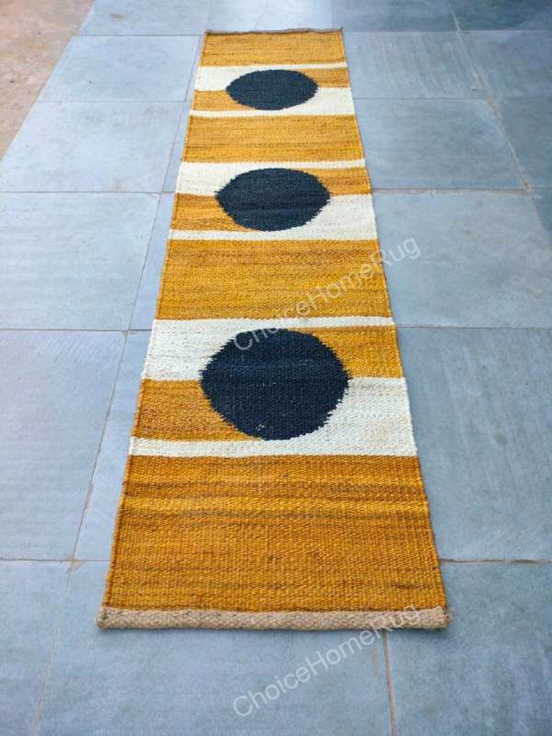 May include: A long, narrow rug with a mustard yellow background and white stripes. Three black circles are woven into the rug, creating a modern geometric pattern.