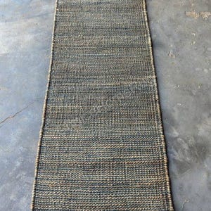 Pode incluir: Um tapete corredor retangular de juta tecida. O tapete apresenta uma paleta de cores naturais com tons de azul e bege. A textura &eacute; vis&iacute;vel, com um padr&atilde;o de tecido apertado. Ideal para corredores ou entradas.