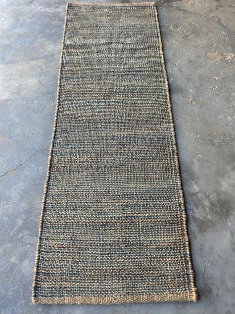 Pode incluir: Um tapete corredor retangular de juta tecida. O tapete apresenta uma paleta de cores naturais com tons de azul e bege. A textura &eacute; vis&iacute;vel, com um padr&atilde;o de tecido apertado. Ideal para corredores ou entradas.