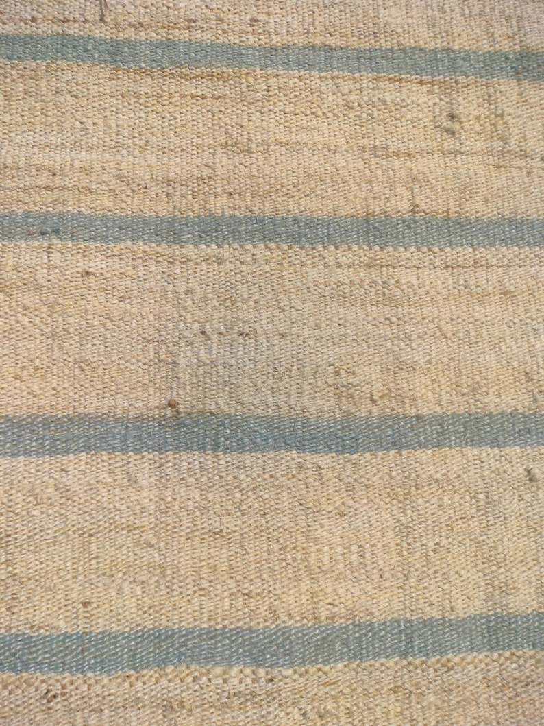 May include: A natural fiber rug with a woven texture and blue stripes. The rug is made of jute and has a rustic look.
