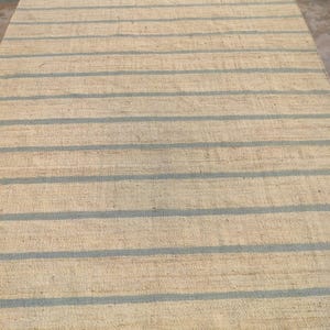 May include: A natural fiber rug with a striped pattern. The rug has a light beige background with blue stripes.