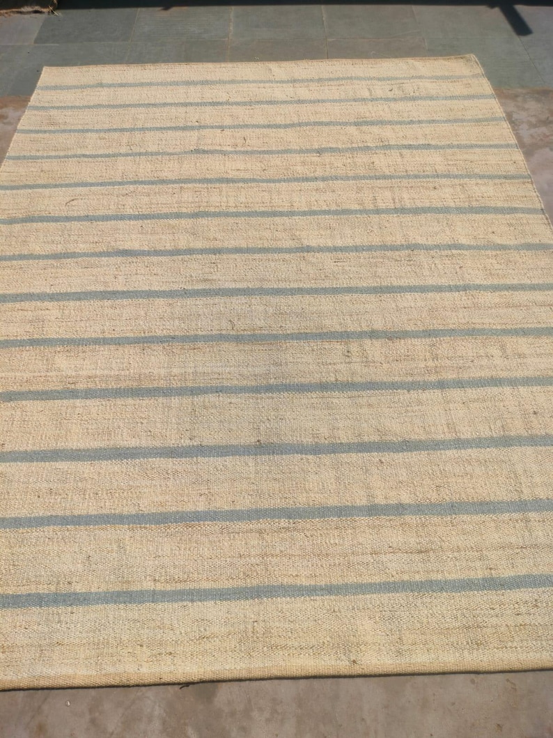 May include: A natural fiber rug with a striped pattern. The rug has a light beige background with blue stripes.