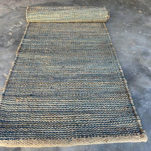 Pode incluir: Um tapete retangular de juta com uma se&ccedil;&atilde;o enrolada na parte superior. O tapete apresenta um design tecido com faixas alternadas de azul e bege natural. O tapete &eacute; adequado para uso interno.