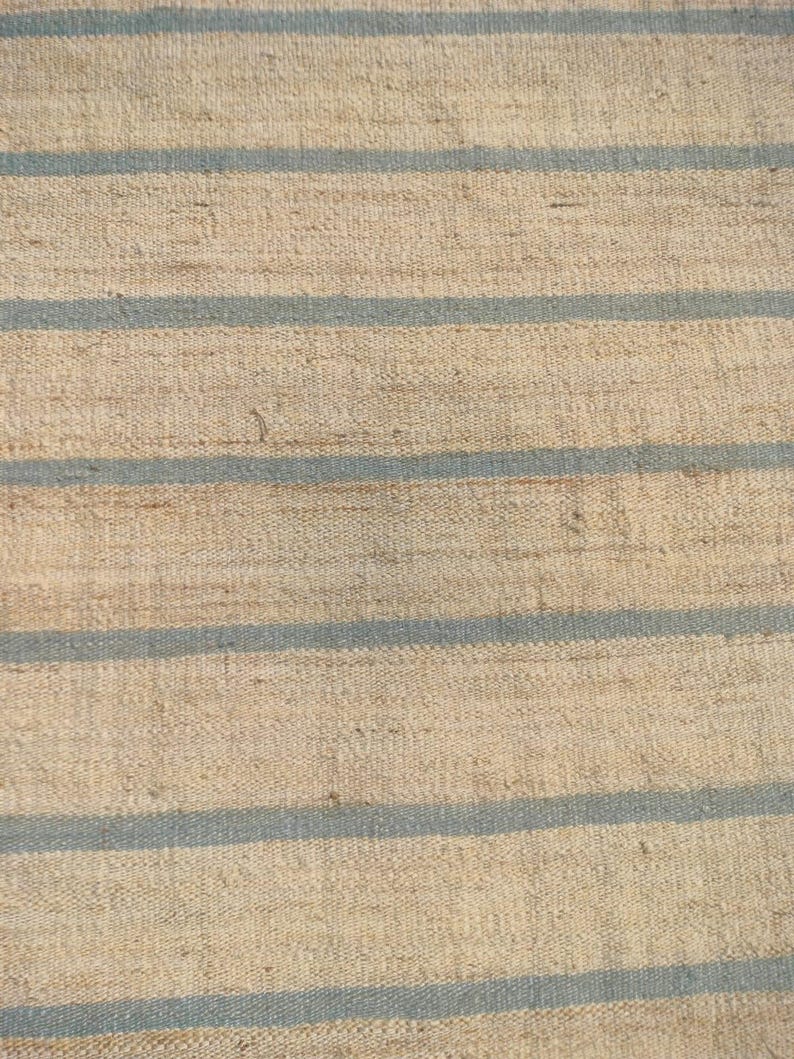 May include: A close-up of a woven rug with horizontal stripes in beige and light blue.