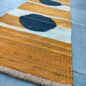 May include: A long, narrow rug with a woven texture. The rug has a mustard yellow background with white stripes and three large black circles.