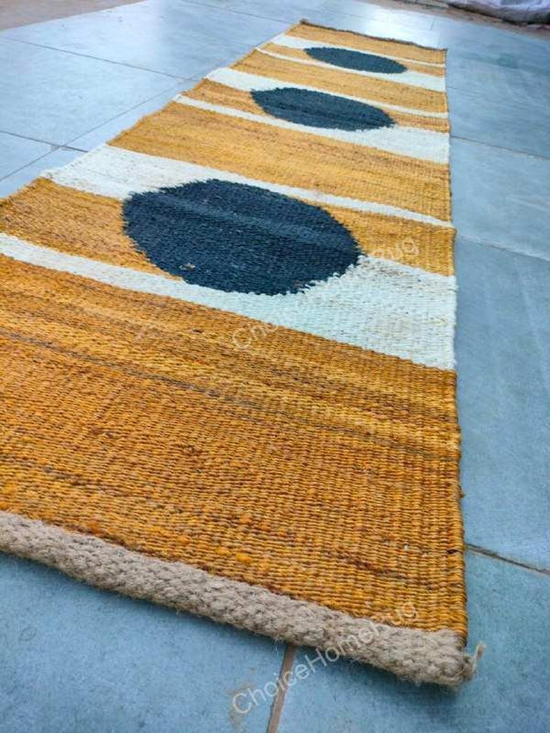 May include: A long, narrow rug with a woven texture. The rug has a mustard yellow background with white stripes and three large black circles.