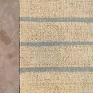 May include: A natural fiber rug with a striped pattern. The rug has a light beige background with blue stripes.
