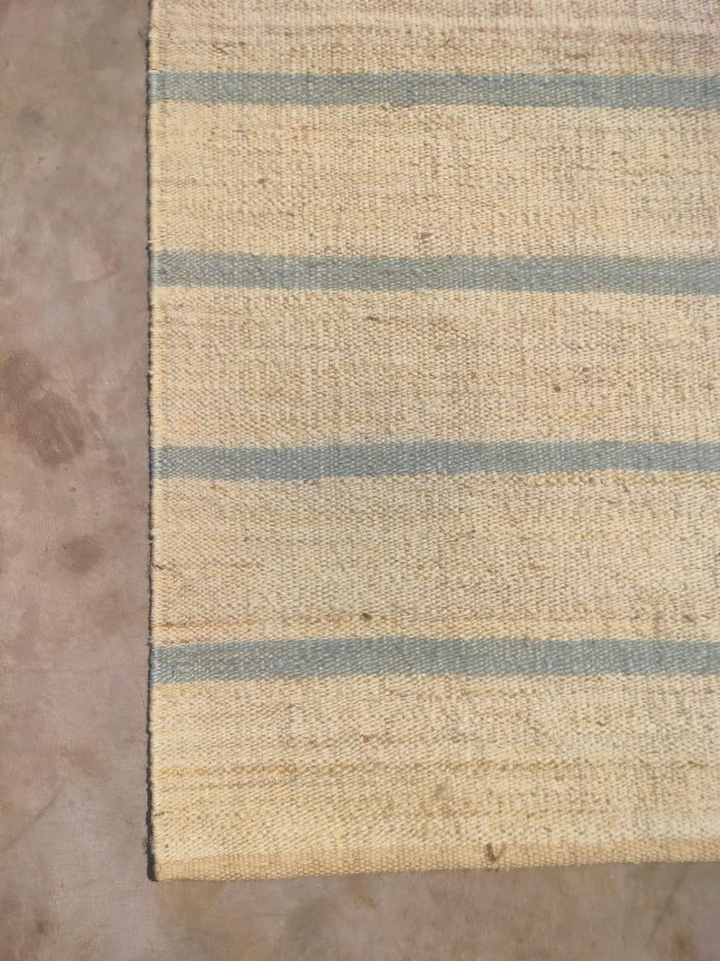 May include: A natural fiber rug with a striped pattern. The rug has a light beige background with blue stripes.