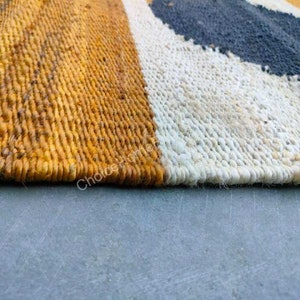 May include: Close-up of a woven rug with stripes of yellow, white, and black. The rug is made of natural fibers and has a textured surface.