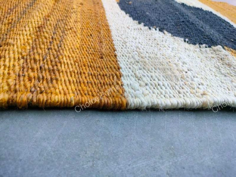 May include: Close-up of a woven rug with stripes of yellow, white, and black. The rug is made of natural fibers and has a textured surface.