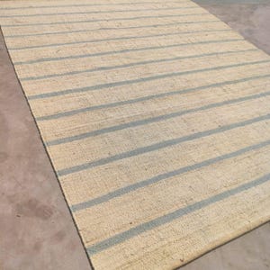 May include: A natural fiber rug with a striped pattern. The rug has a light beige background with blue stripes.