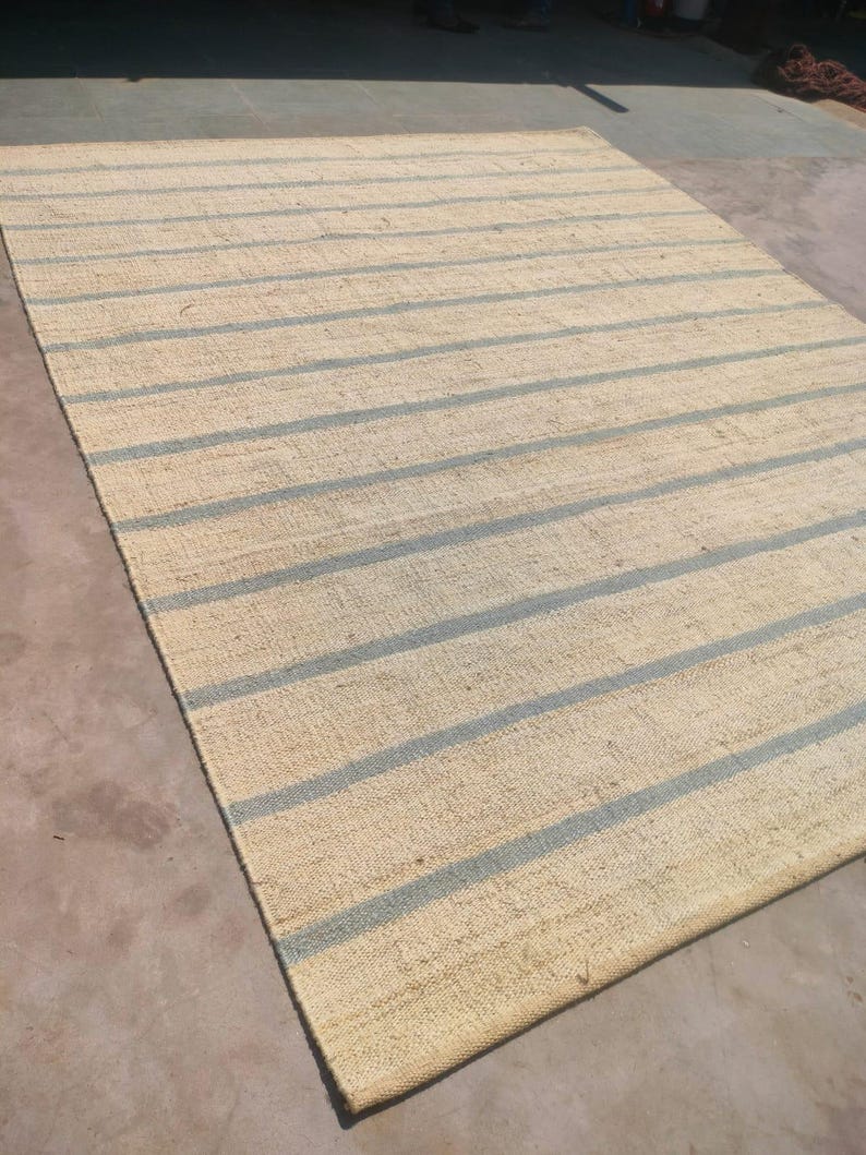 May include: A natural fiber rug with a striped pattern. The rug has a light beige background with blue stripes.
