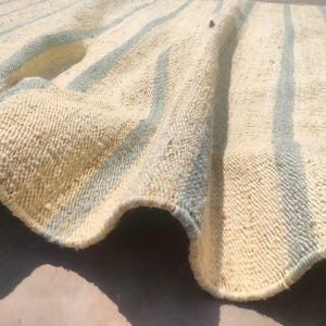 May include: A close-up of a cream-colored rug with blue stripes. The rug is woven and has a textured surface.