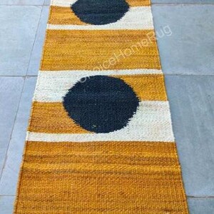 May include: A long, narrow, mustard yellow and white striped rug with black circles. The rug has a jute border.