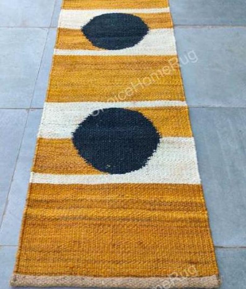 May include: A long, narrow, mustard yellow and white striped rug with black circles. The rug has a jute border.