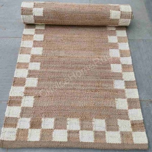 K&ouml;nnte beinhalten: Ein brauner und wei&szlig;er karierter Jute-Teppich mit gewebtem Muster. Der Teppich ist aufgerollt und hat einen Fransenrand.