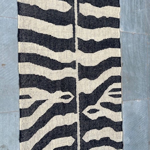 May include: A rectangular woven textile runner featuring a high-contrast black and cream zebra stripe pattern. The design consists of organic, irregular horizontal bands that mirror each other across a central vertical seam, creating a symmetrical look.