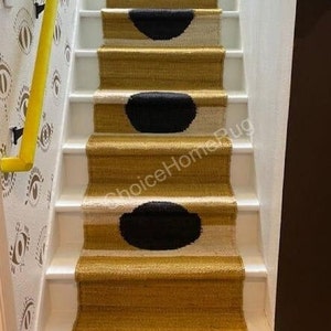 May include: A set of stairs with a black and white patterned rug runner. The rug has a yellow background with black circles and white accents. The stairs are white with a yellow handrail.