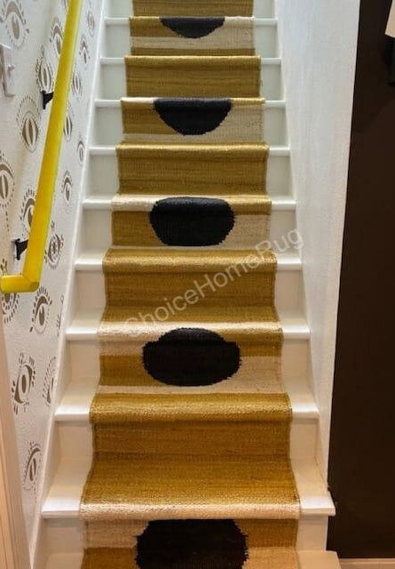 May include: A set of stairs with a black and white patterned rug runner. The rug has a yellow background with black circles and white accents. The stairs are white with a yellow handrail.