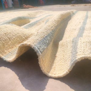 May include: A white and blue striped rug with a woven texture. The rug is folded in half and the blue stripes are visible on the edges.
